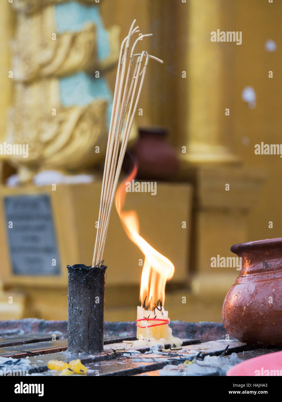 Räucherstäbchen und ein Bündel von Kerzen brennen im Morgengrauen vor einem goldenen Stupa an der Shwedagon-Pagode in Yangon, Myanmar. Stockfoto