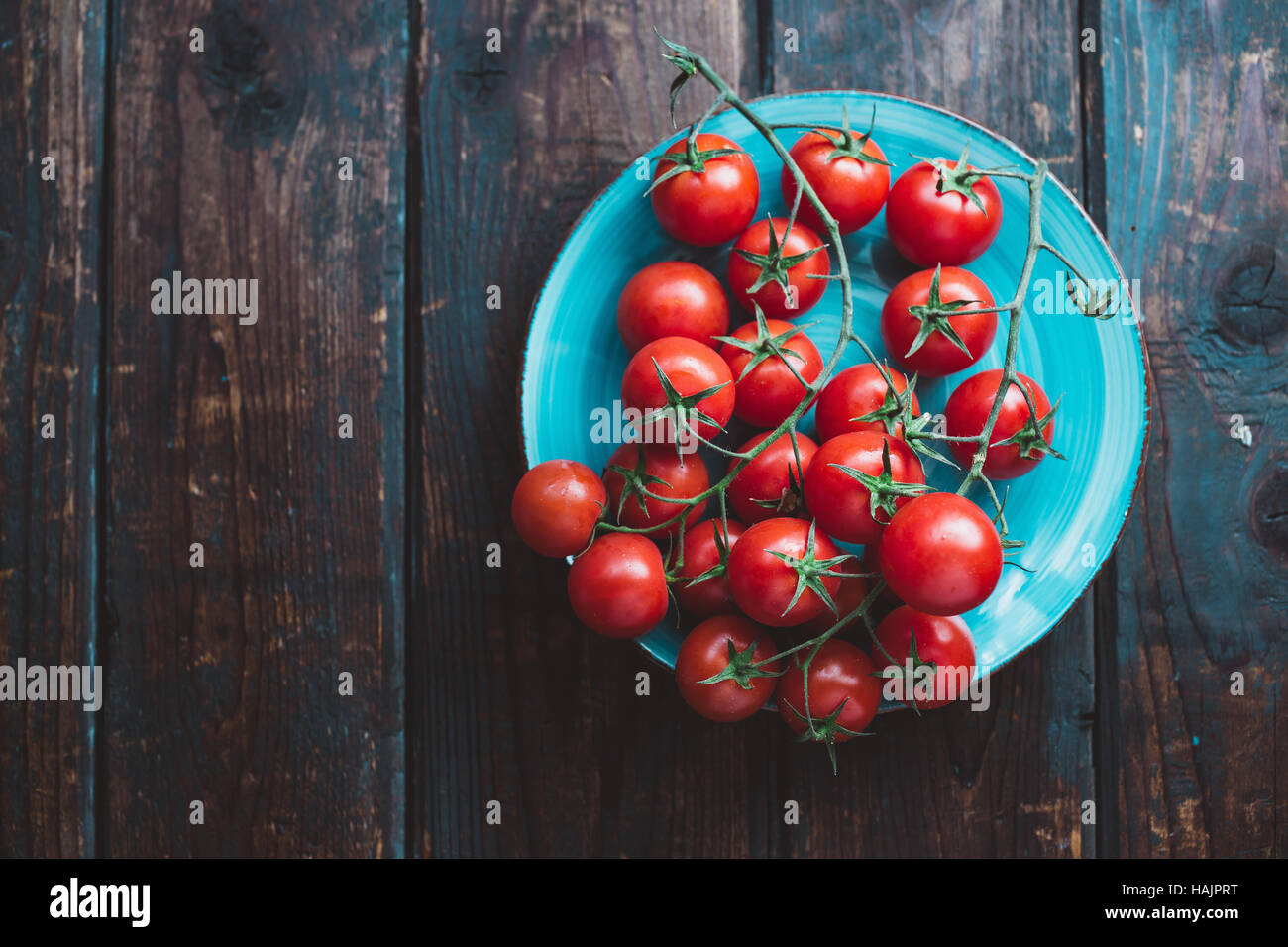 Cherry-Tomaten am Rebstock. Blaue Teller mit Cherry-Tomaten auf Holztisch. Stockfoto