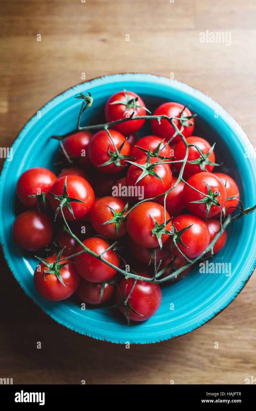Cherry-Tomaten am Rebstock. Blaue Schale Cherrytomaten auf Holztisch. Stockfoto
