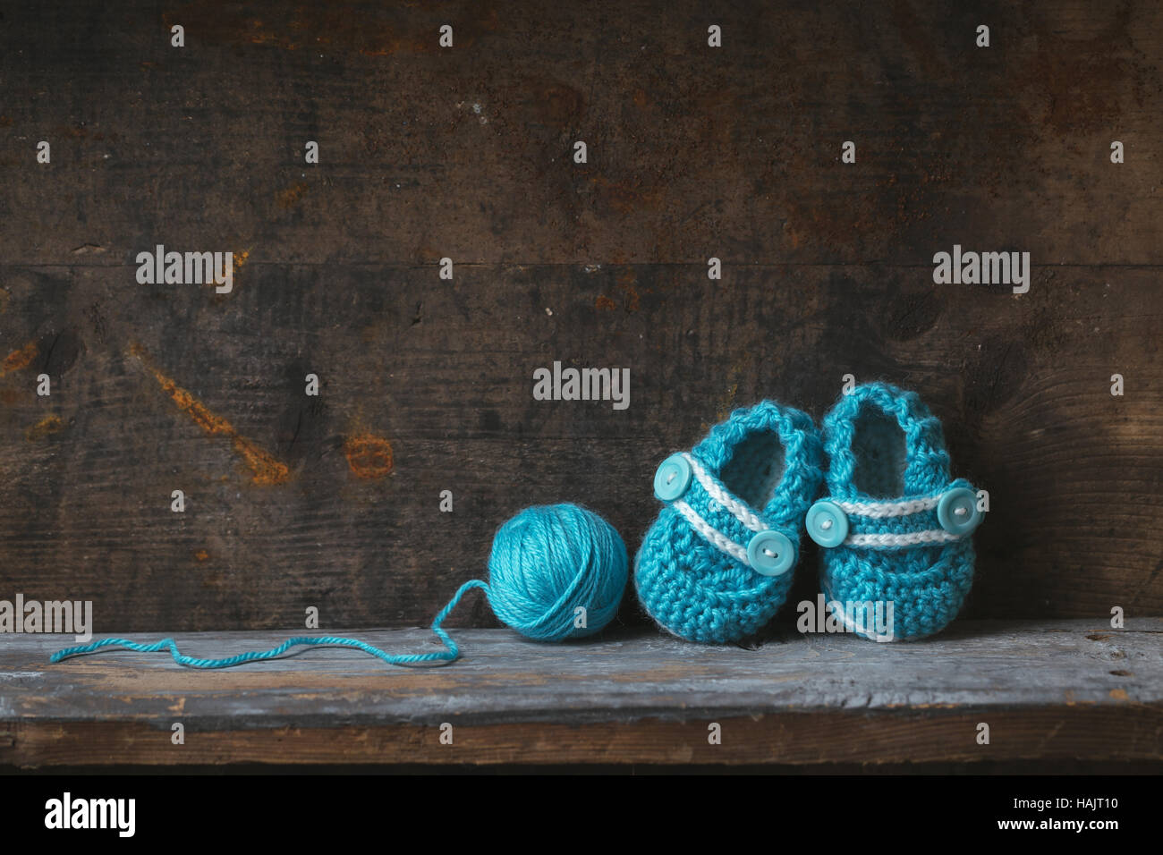 Gehäkelte Babyschuhe mit blauem Garn auf einem Holzregal. Stockfoto