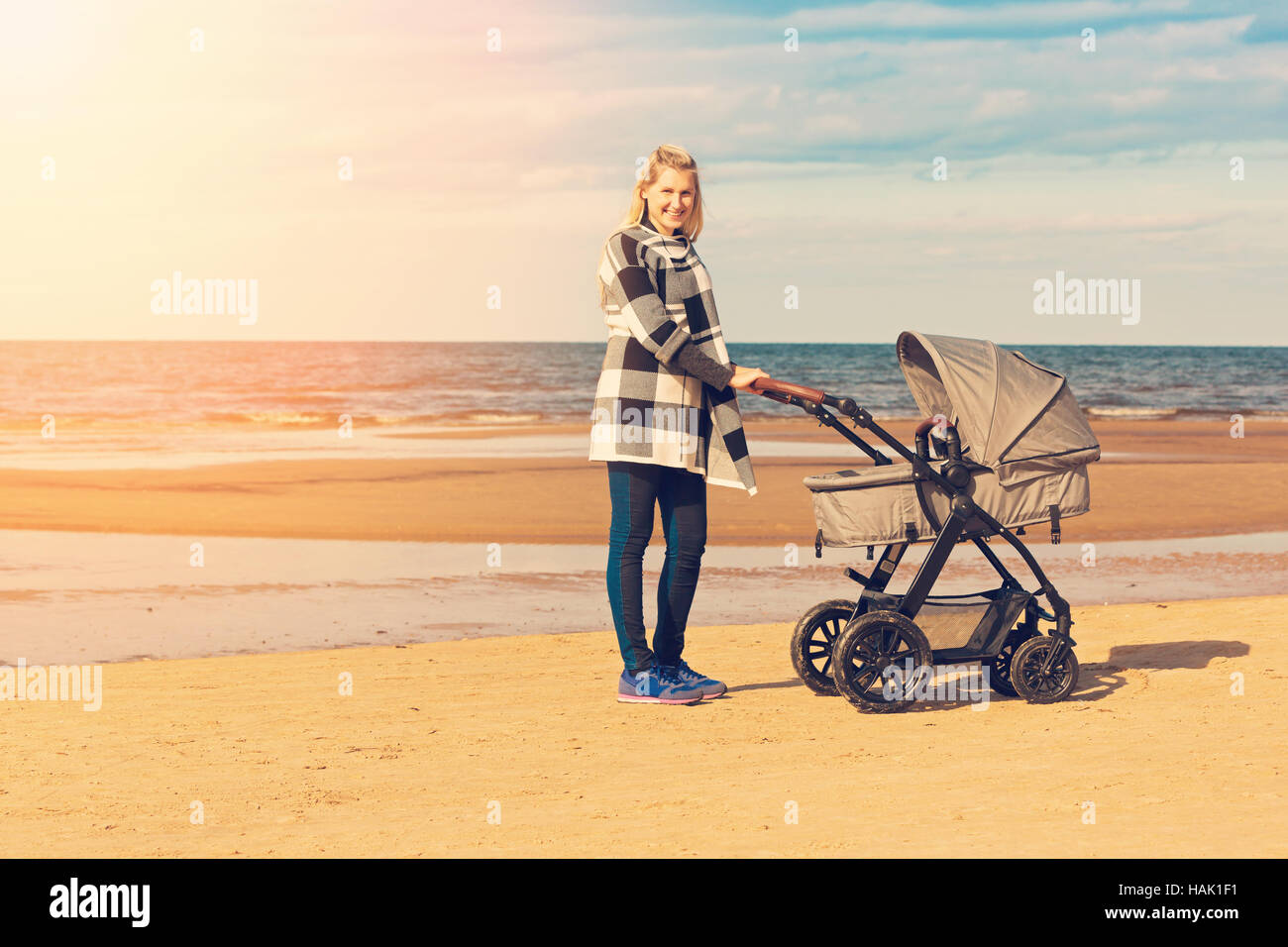 lächelnde junge Mutter mit Kinderwagen am Strand Stockfoto