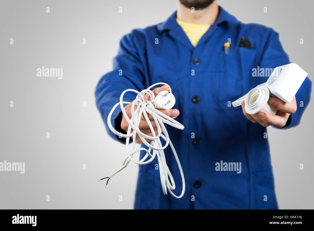 Elektriker mit Ausrüstung in den Händen isoliert auf grau Stockfoto
