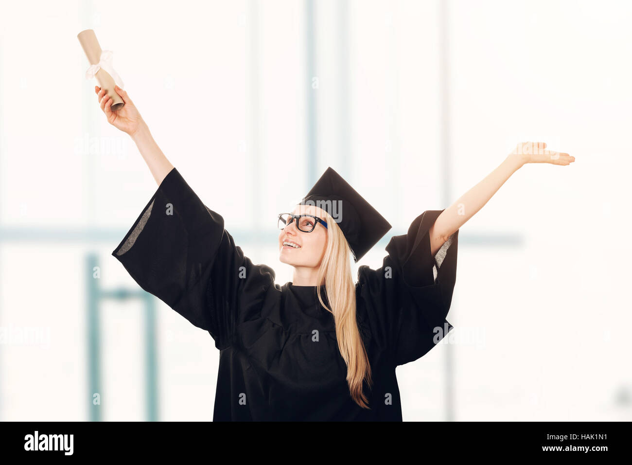 glücklich Hochschulabsolvent trägt Mütze und Mantel und Diplom in der hand hält Stockfoto