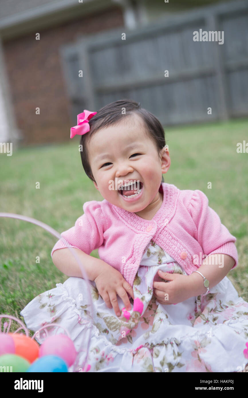 Porträt von Kleinkind Mädchen tragen rosa und sitzen auf dem Rasen lachend mit Osternest im Hinterhof Stockfoto