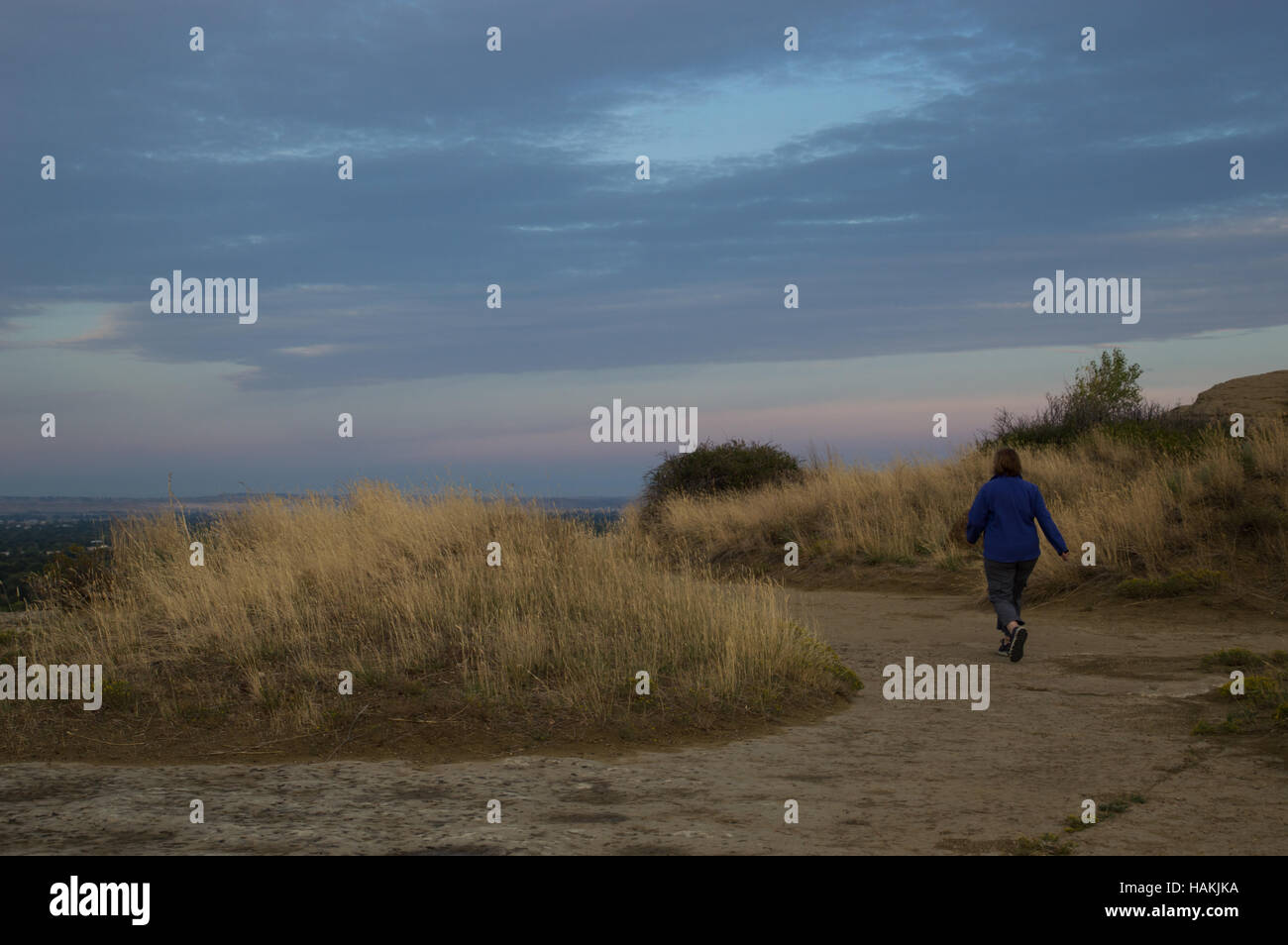 Eine Frau trägt eine blaue Kornblume-Jacke mit ihr zurück in die Kamera zu Fuß zügig in Richtung Sandstein Felsen bei Sonnenaufgang Stockfoto