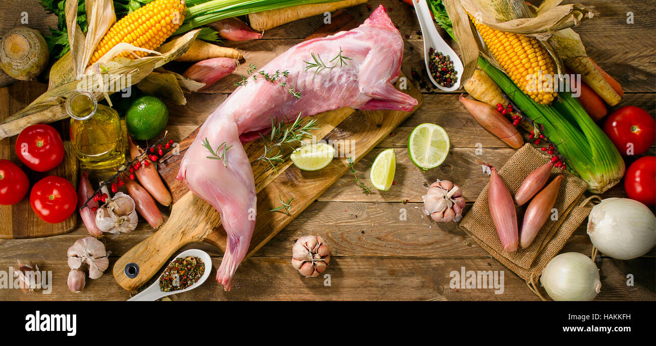 Rohe ganzes Kaninchen mit Gemüse und Gewürzen auf dunklem Hintergrund rustikal. Ansicht von oben Stockfoto