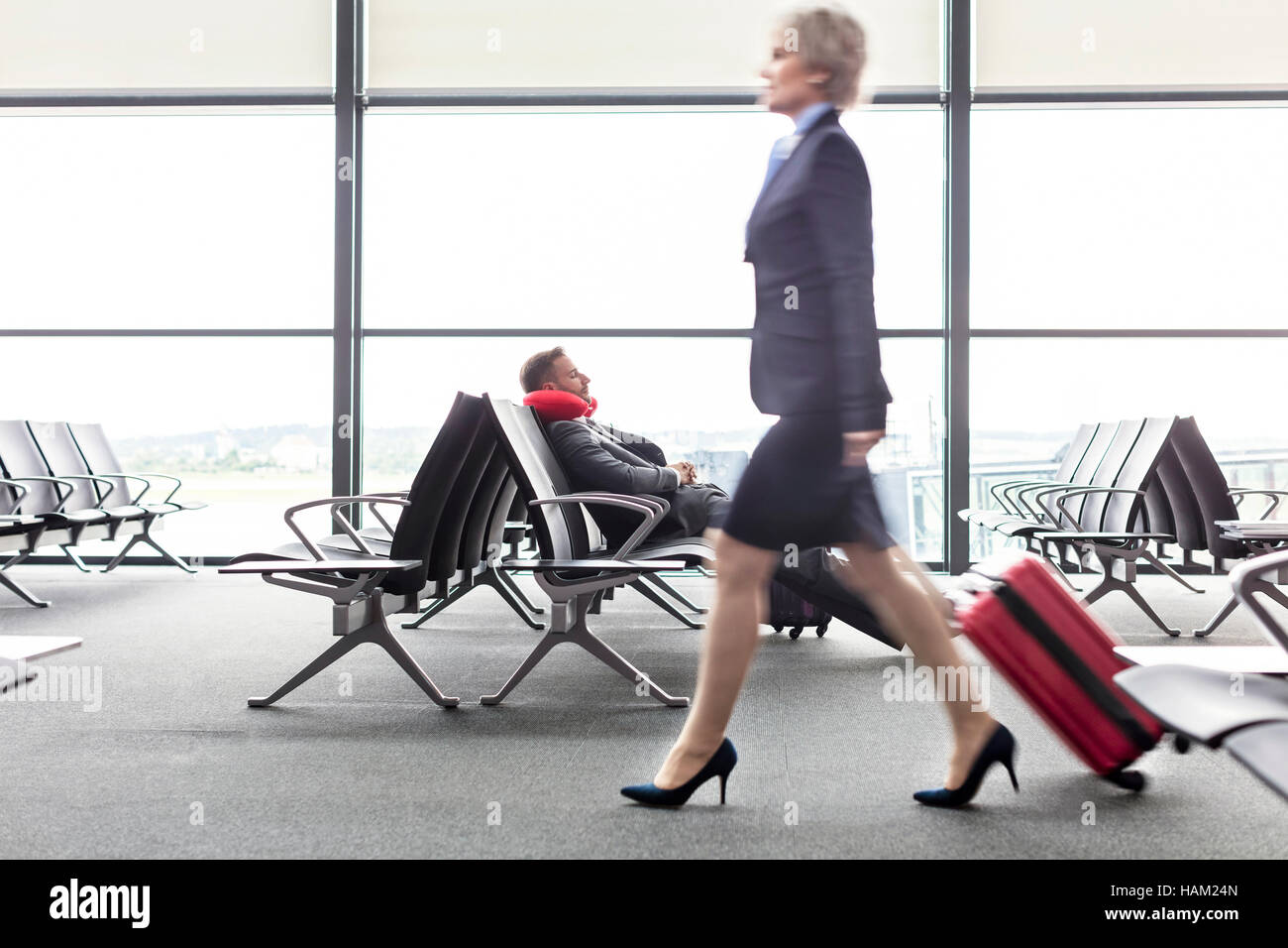 Geschäftsfrau ziehen Koffer Vergangenheit ruhen Geschäftsmann mit Nackenkissen im Abflugbereich des Flughafen Stockfoto