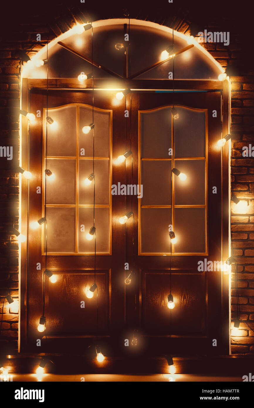 Schöne alte Holztür mit leuchtenden Lampen geschmückt. Weihnachten Hintergrund Stockfoto