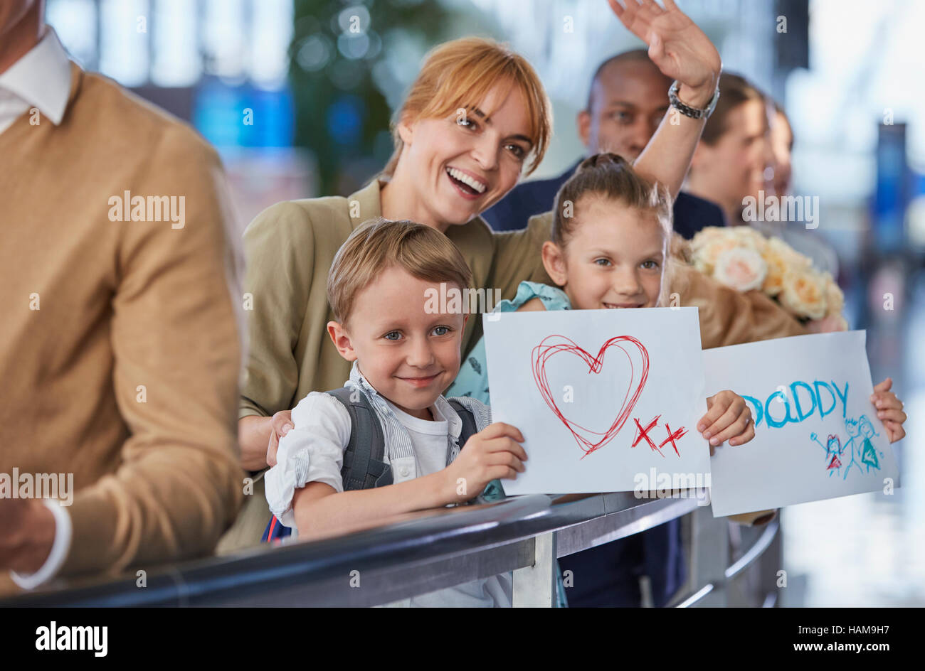 Mutter und Kinder mit Willkommen Schilder für Vater am Flughafen Stockfoto