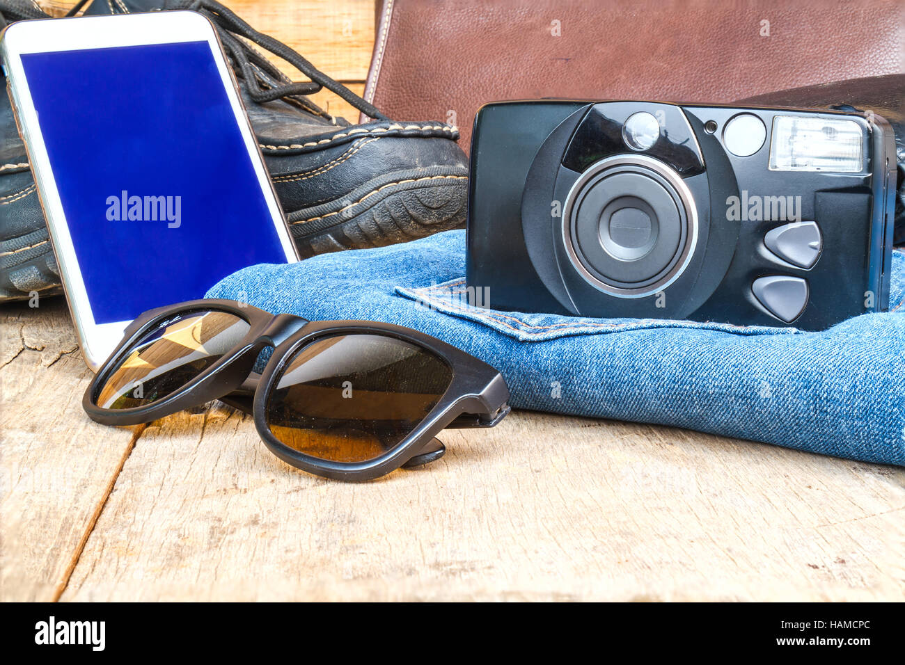 Reisen Sie casual-Outfits mit Kamera, Smartphone, Schuhe, Geldbörse, Ledertasche, Sonnenbrille und Jean auf Holztisch. Reisekonzept. Stockfoto