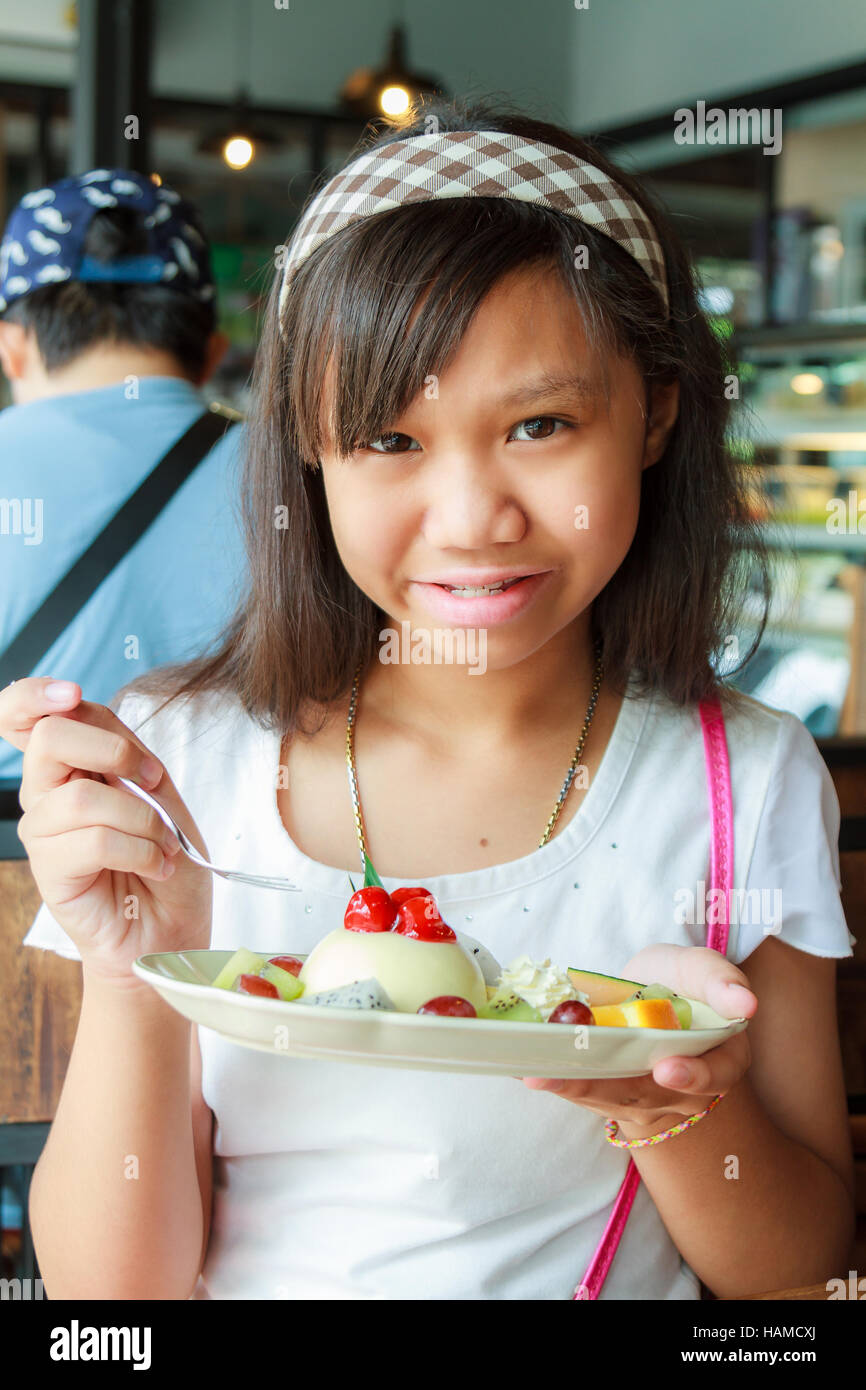Asien Mädchen essen Käsekuchen mit Kirsche, Kiwi, Orangen und Trauben im Restaurant. Stockfoto
