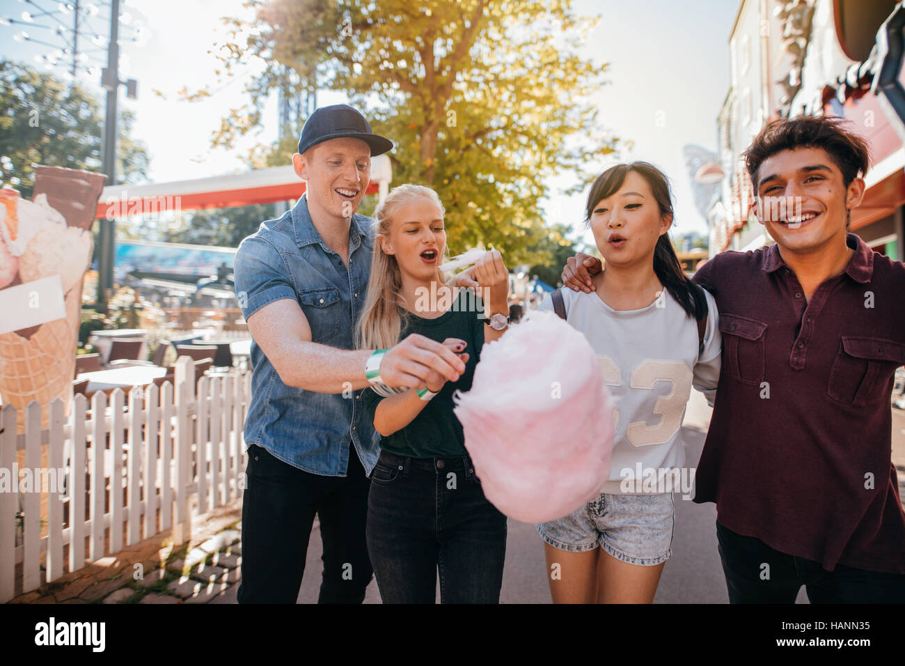 Gruppe von Freunden essen Zuckerwatte im Vergnügungspark. Junge Männer und Frauen teilen Baumwolle Zuckerwatte am Festplatz. Stockfoto