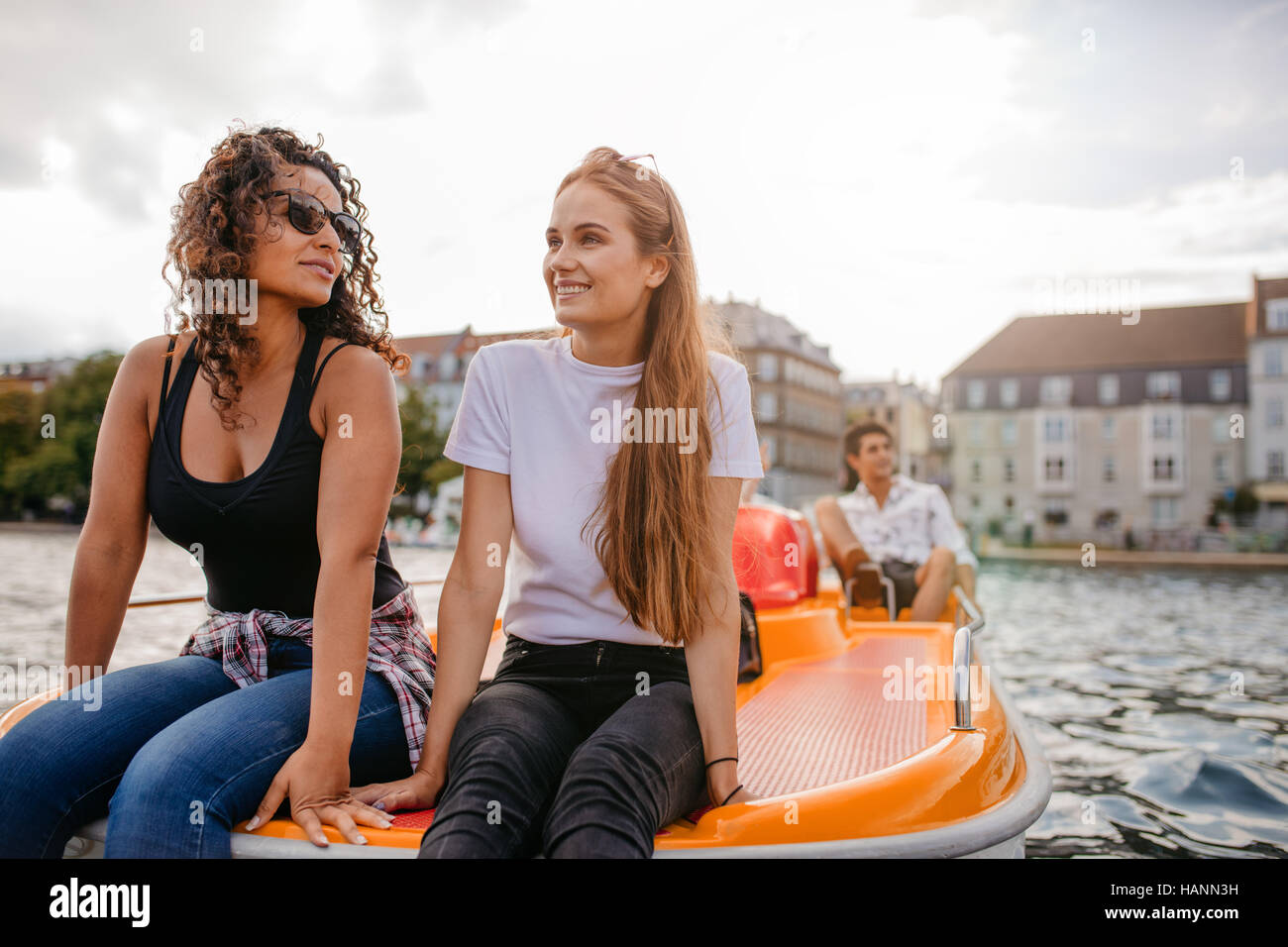 Schuss der Teenager Frauen sitzen auf Tretboot mit einem Mann im Hintergrund. Glückliche junge Freunde genießen, Bootfahren im See. Stockfoto