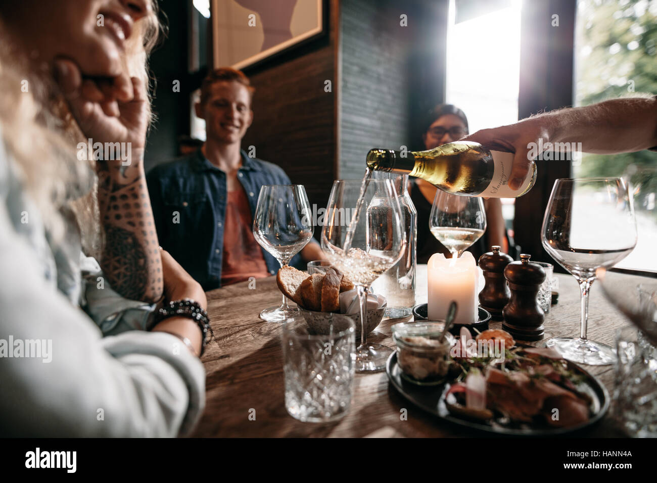 Mann Hand strömenden Weißwein aus der Flasche in Gläser mit Freunden am Tisch sitzen. Gruppe von jungen Menschen mit Essen und Getränken bei restau Stockfoto
