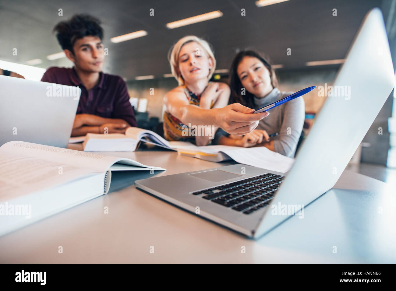 Multirassische Jugendliche, die Gruppenstudien am Tisch machen, mit Frau, die auf den Laptop zeigt. universitätsstudenten, die Informationen für ihr Projekt recherchieren. Stockfoto
