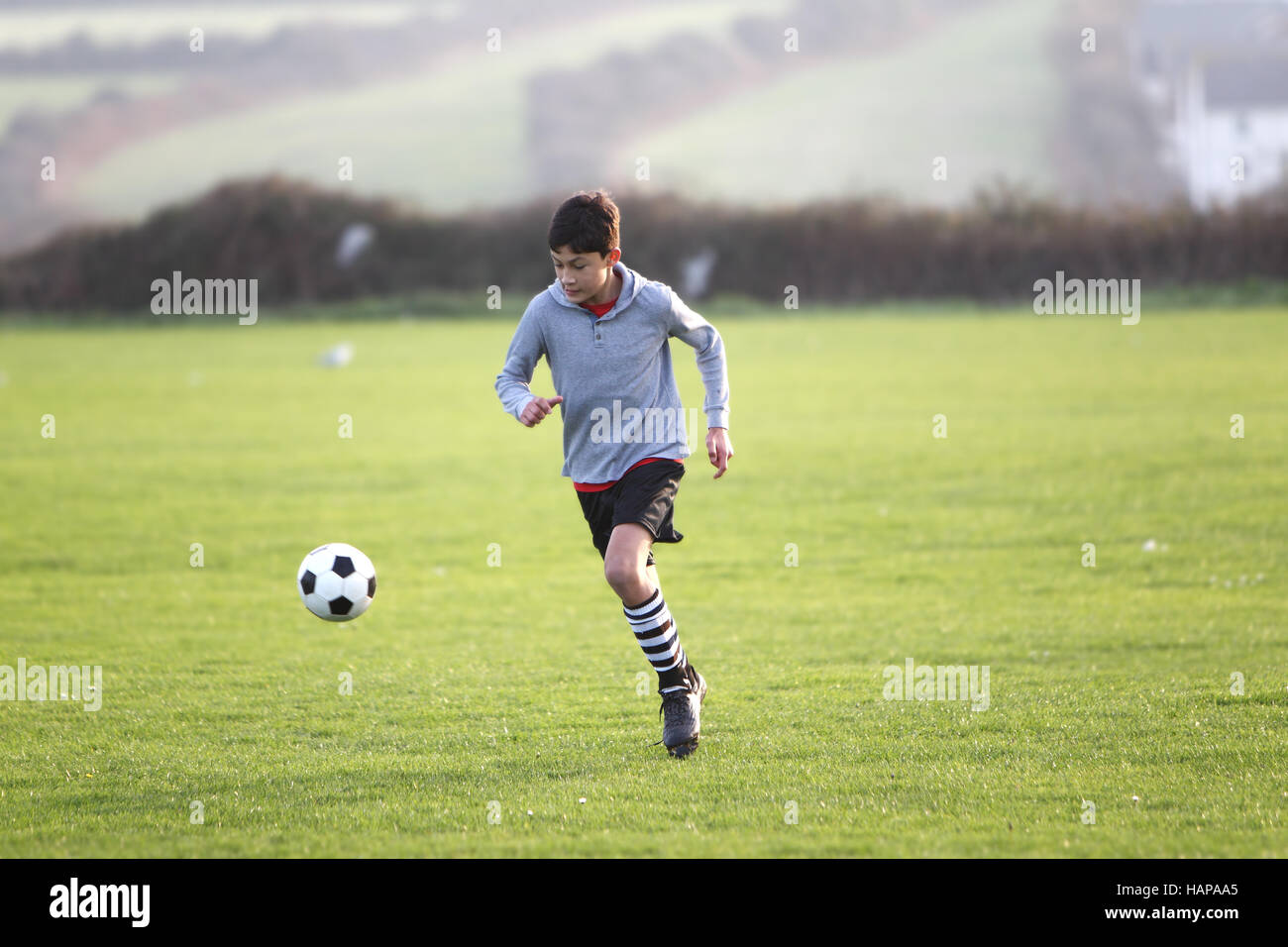 Junge mit Fußball außerhalb der goldenen Stunde bei Sonnenuntergang Stockfoto