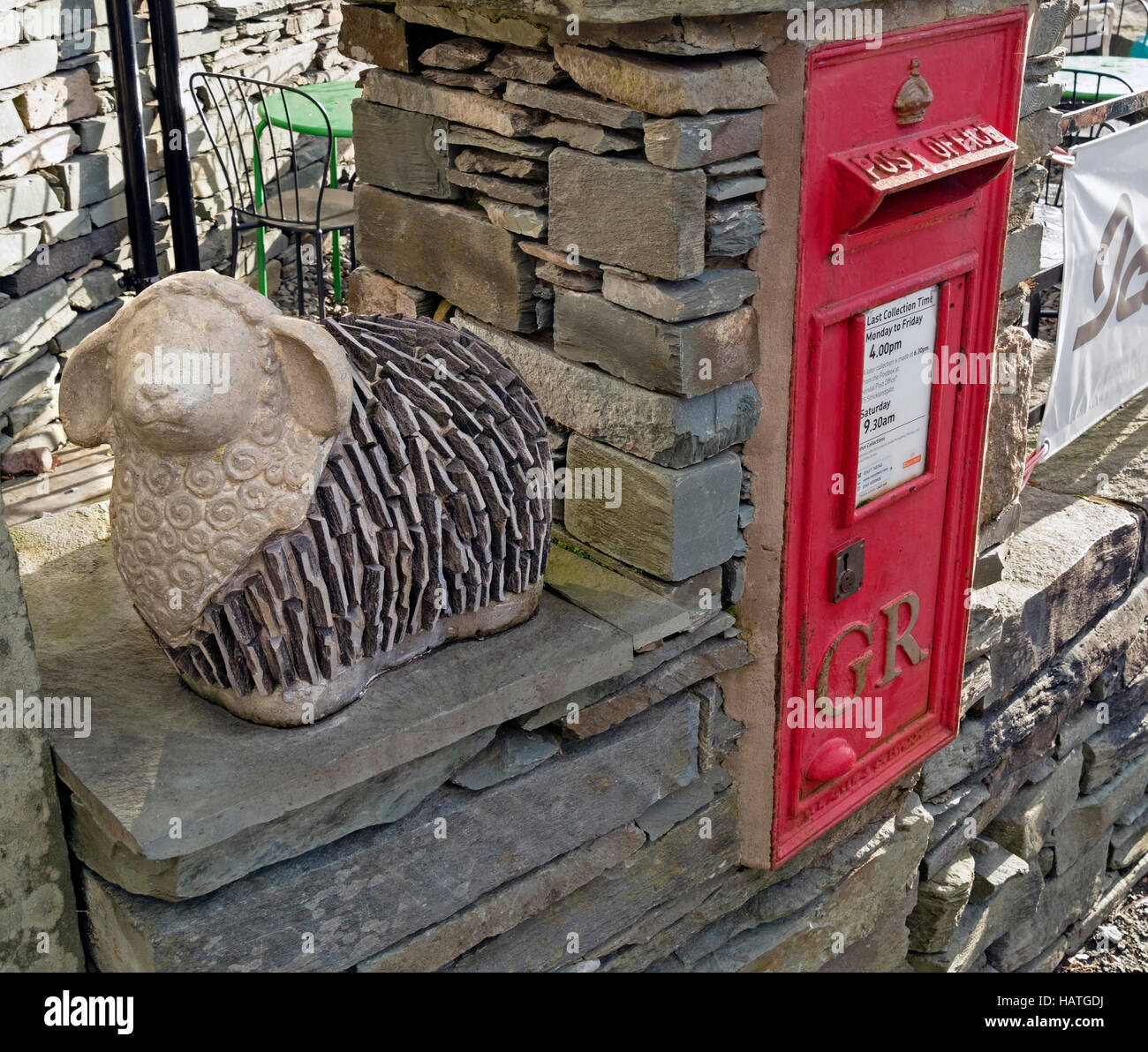 Roter Briefkasten in einer Schieferwand mit Lakeland-Schafskulptur, Elterwater, English Lake District, Cumbria, Großbritannien. Stockfoto
