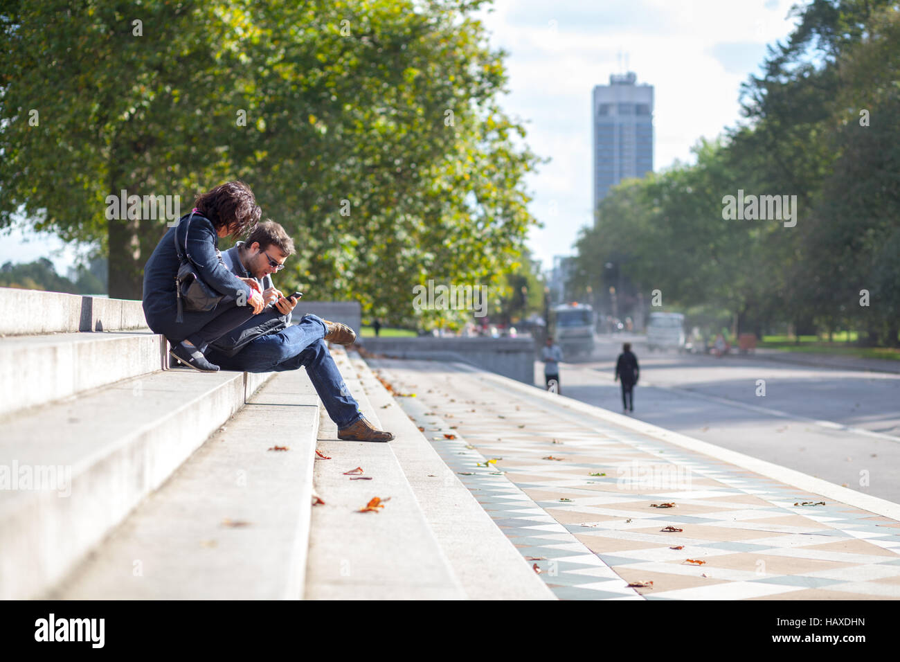 London Park, paar sitzt auf der Treppe und SMS auf dem Handy Stockfoto