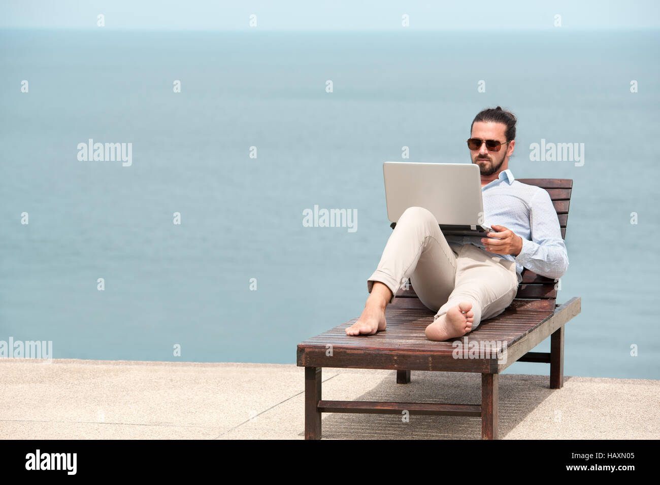 Geschäftsmann in einem Anzug auf Liegestuhl Eingabe Laptop am Strand Stockfoto
