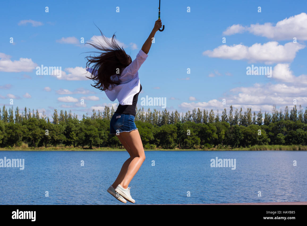 Glückliche junge Frau springen über blauen Himmel auf der Bank am Pool im Garten. Stockfoto