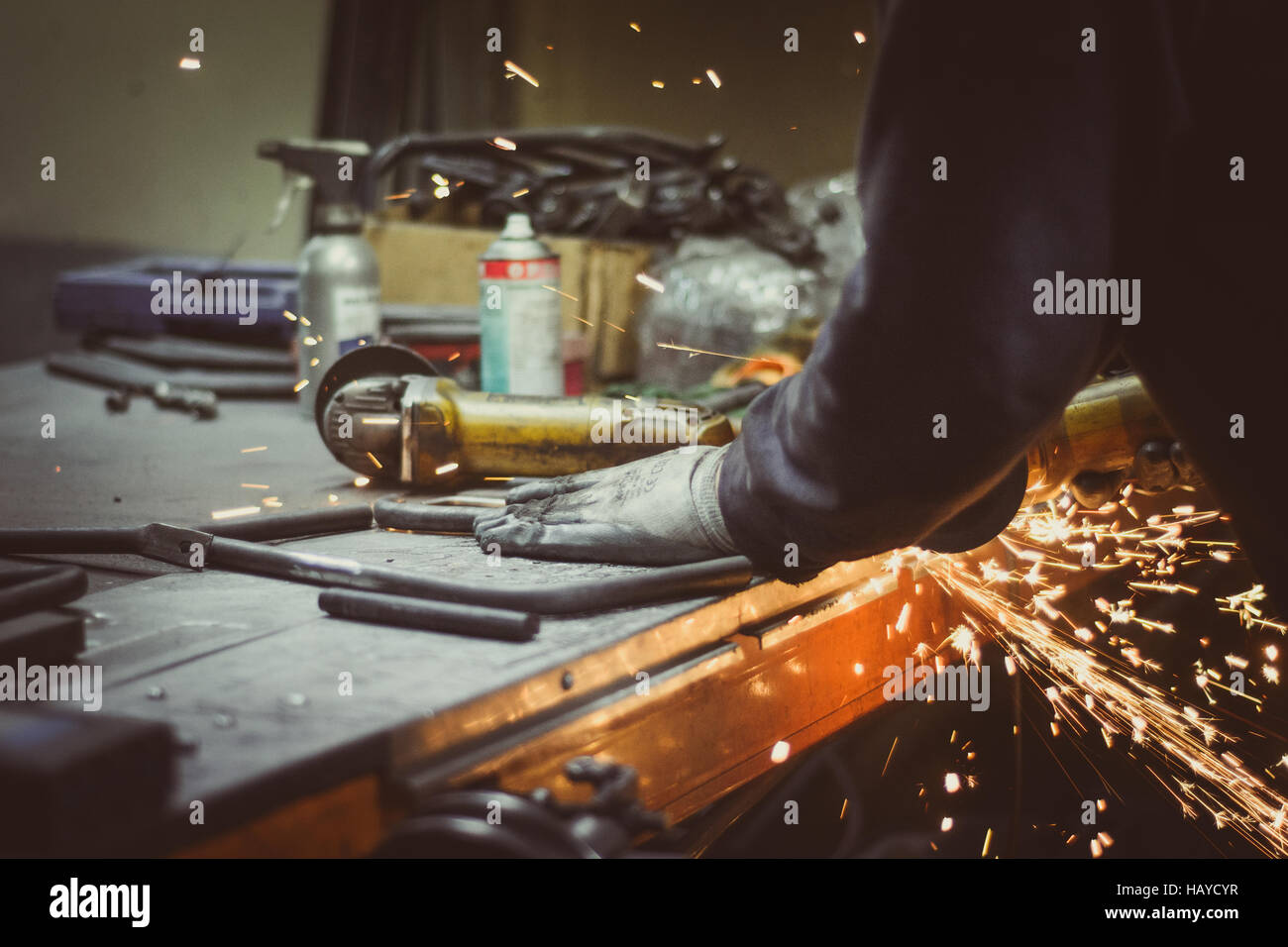 Arbeiter schneiden Stück Rundrohr mit einem Winkelschleifer auf einem Werkstatt-Tisch, Funken produzieren Stockfoto