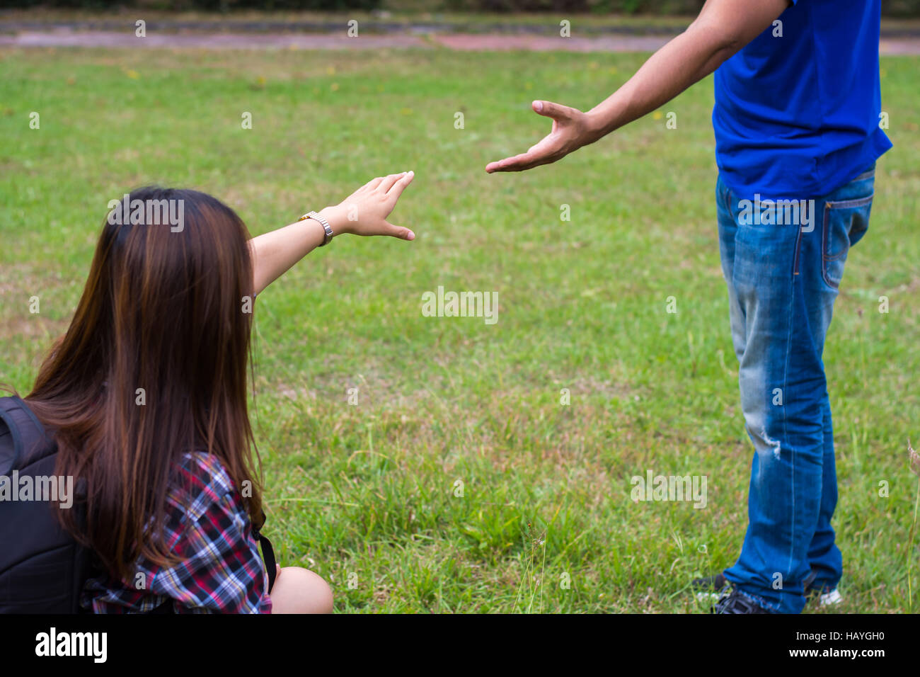 Frau sitzt auf dem Rasen um die Hand des Menschen zu erreichen. Hand und Liebe Konzept zu helfen. Stockfoto
