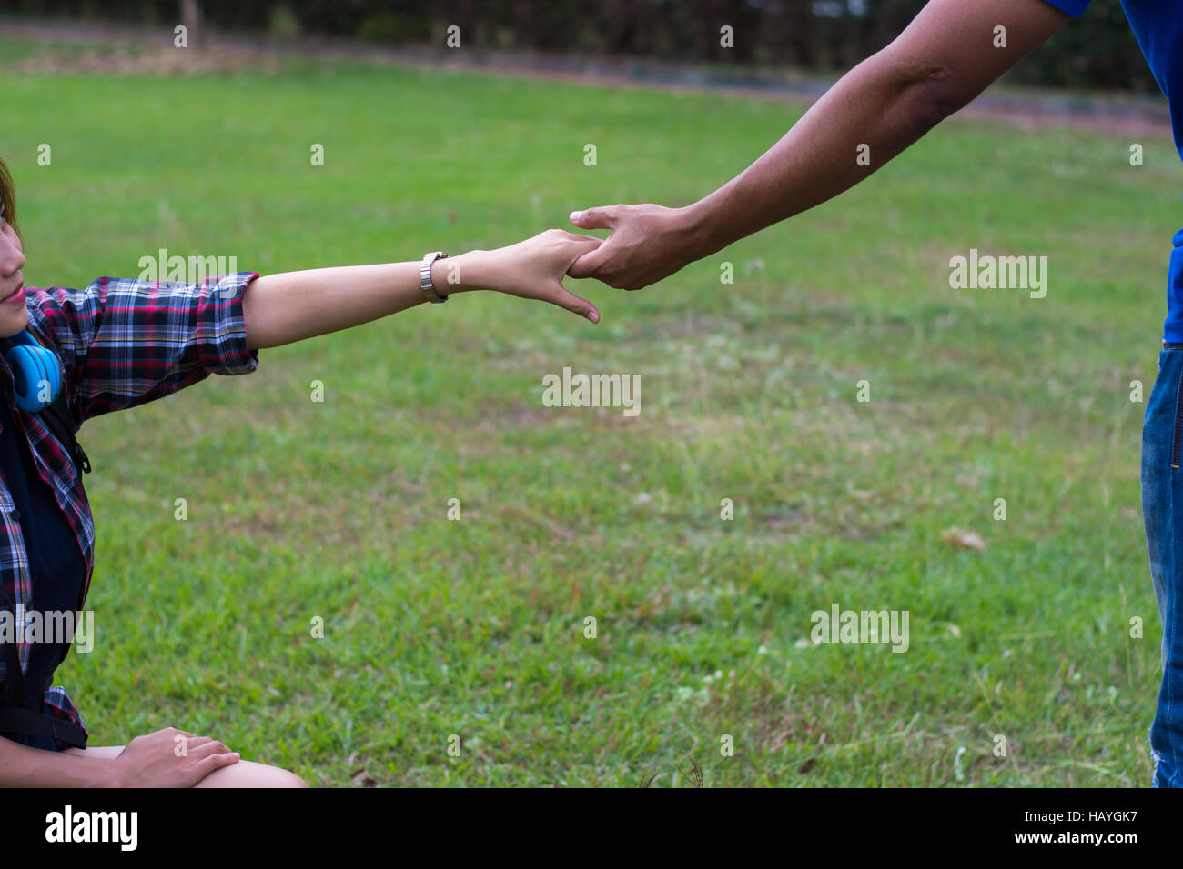 Frau sitzt auf dem Rasen um die Hand des Menschen zu erreichen. Hand und Liebe Konzept zu helfen. Stockfoto