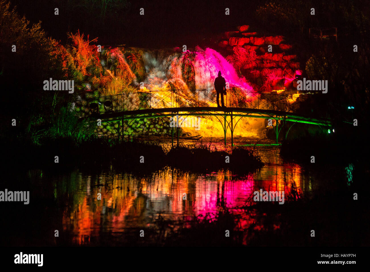 Eine einzelne Person steht im Silhouette in den Gärten der Blenheim Palace als der Wasserfall, die, den ich oben mit festlichen Lichtern für die Weihnachtszeit, bekannt als der beleuchteten Wasserfall "Cascade" Schlitz. Stockfoto