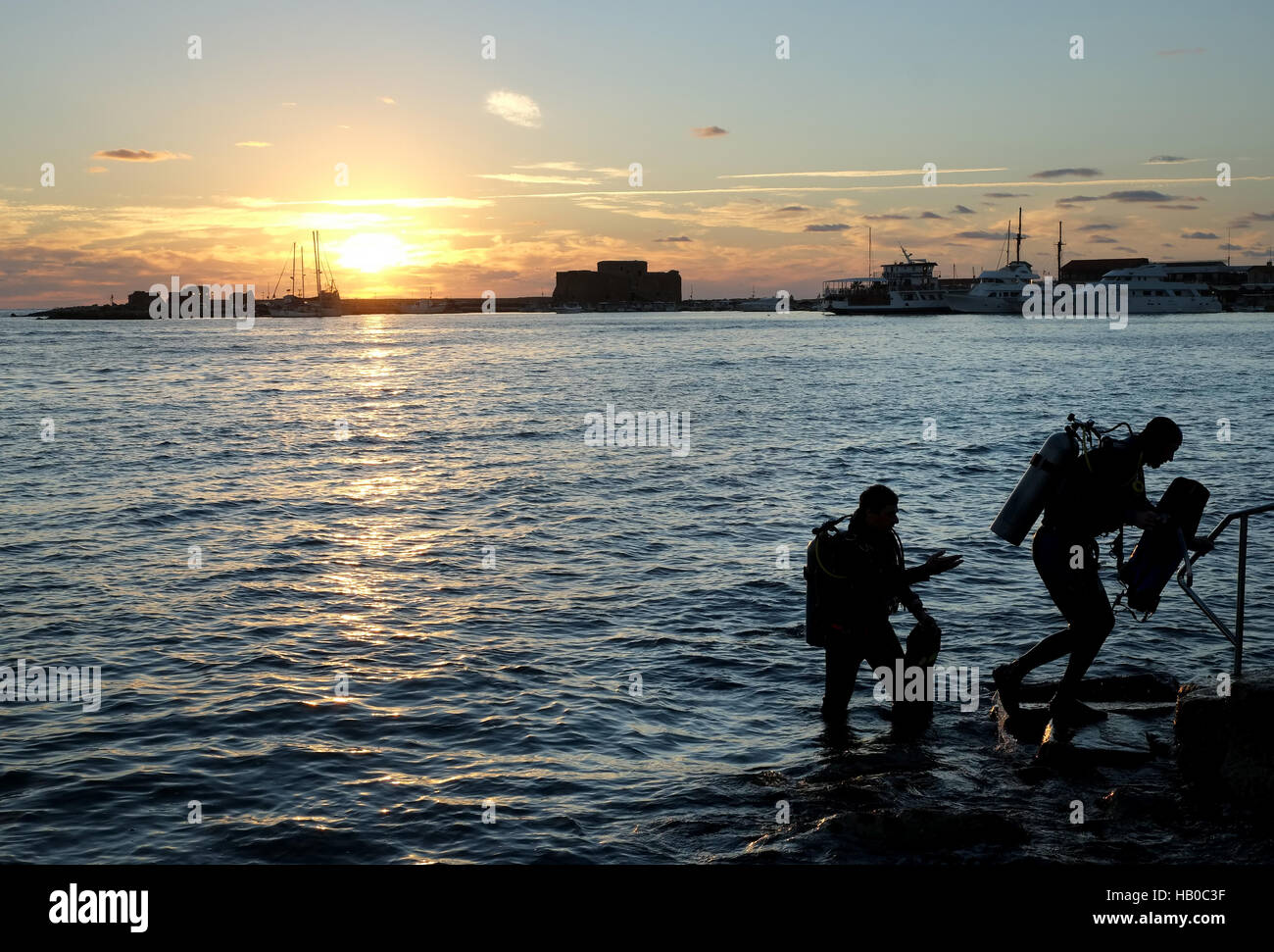 Cydive Tauchlehrer und Schüler verlassen das Wasser bei Sonnenuntergang nach einem Tauchgang an der Uferpromenade im Hafen von Paphos. Stockfoto