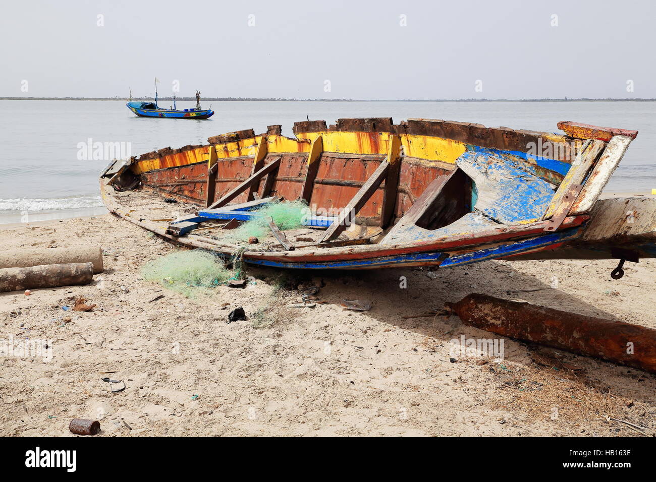 Alte hölzerne Colorist Angelboot/Fischerboot unter am Morgen Sonne ruiniert und kaput gestrandet auf dem Sand des Strandes mit Blick auf die Flussmündung der Casamance. Stockfoto