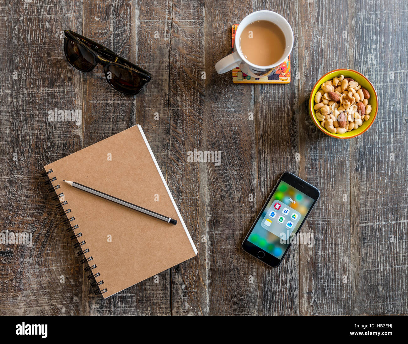 Smartphone, Notebook mit Stift, Sonnenbrille, Kaffee und Nüssen, snacks auf einem Holztisch Stockfoto