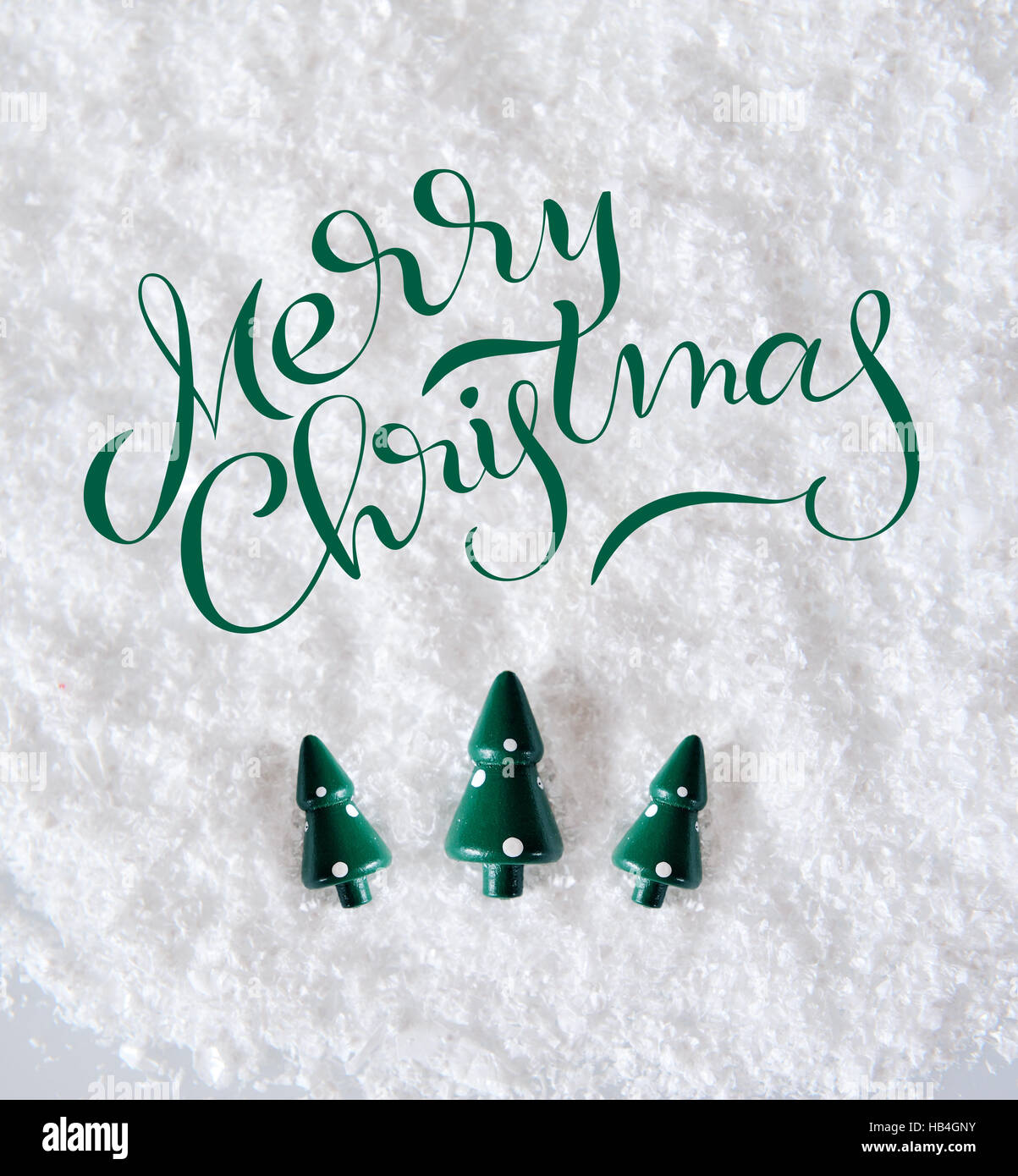 Drei Miniatur-Bäume auf Schnee mit Text Frohe Weihnachten. Kalligraphie-Schriftzug Stockfoto