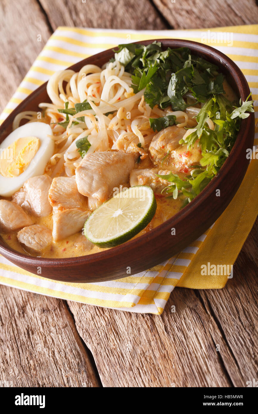 Malaysische Laksa Suppe mit Huhn, Ei, Nudeln und Kräutern hautnah in einer Schüssel auf dem Tisch. vertikale Stockfoto