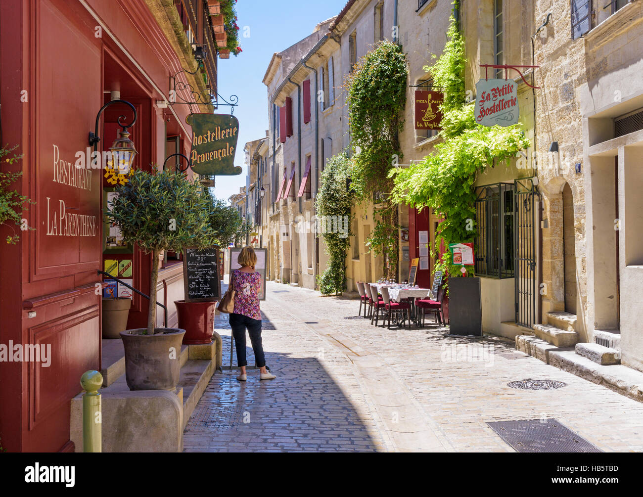Frau auf der Suche auf einer Speisekarte in einer malerischen Straße innerhalb der mittelalterlichen Stadt Uzès, Gard, Frankreich Stockfoto