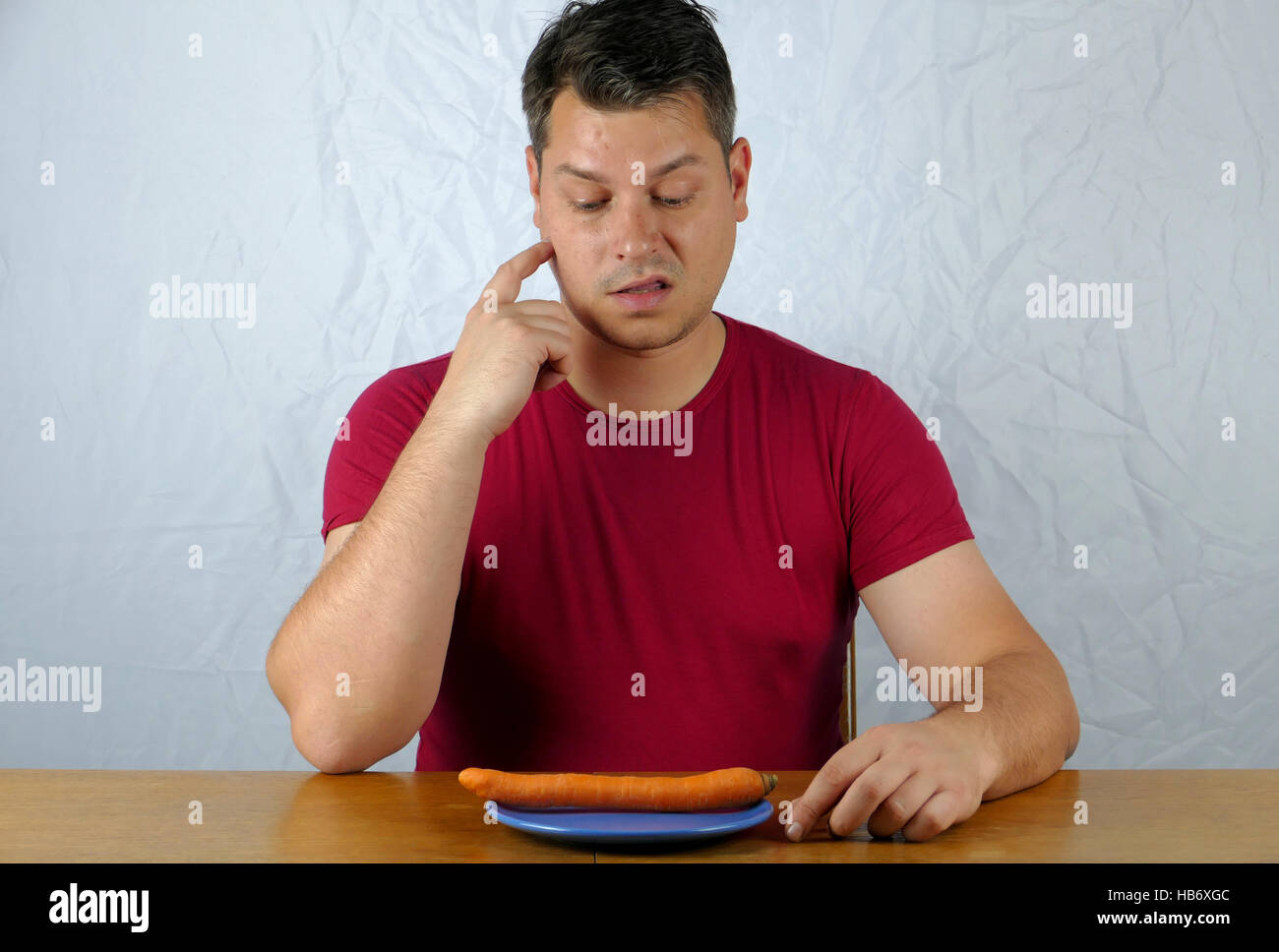 Junger Mann Abneigung Karotte am Teller, gesunde Food-Konzept. Stockfoto