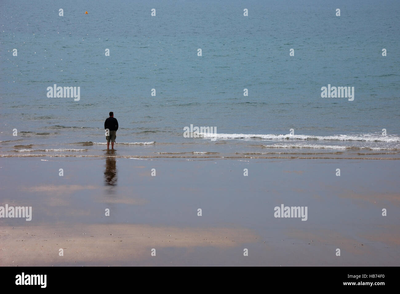 Einsamer Mann in kurzen Hosen Stand am Rande des Strandes mit Blick auf Meer Stockfoto