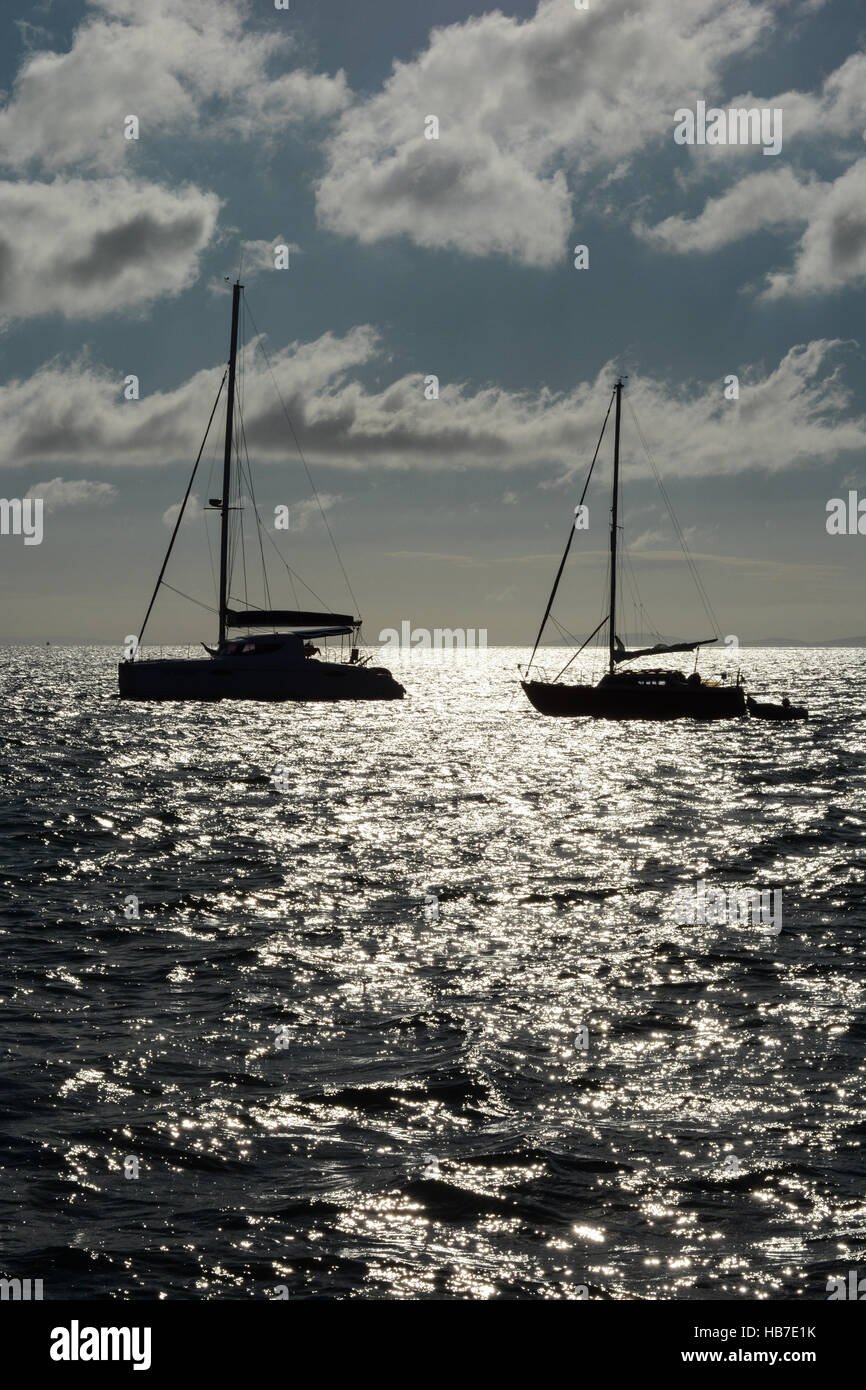 Zwei Yachten in Tenby Bucht früh an einem Sommermorgen verankert. Blauer Himmel mit weißen flauschigen Wolken und die Sonne auf dem Meer reflektiert. Stockfoto