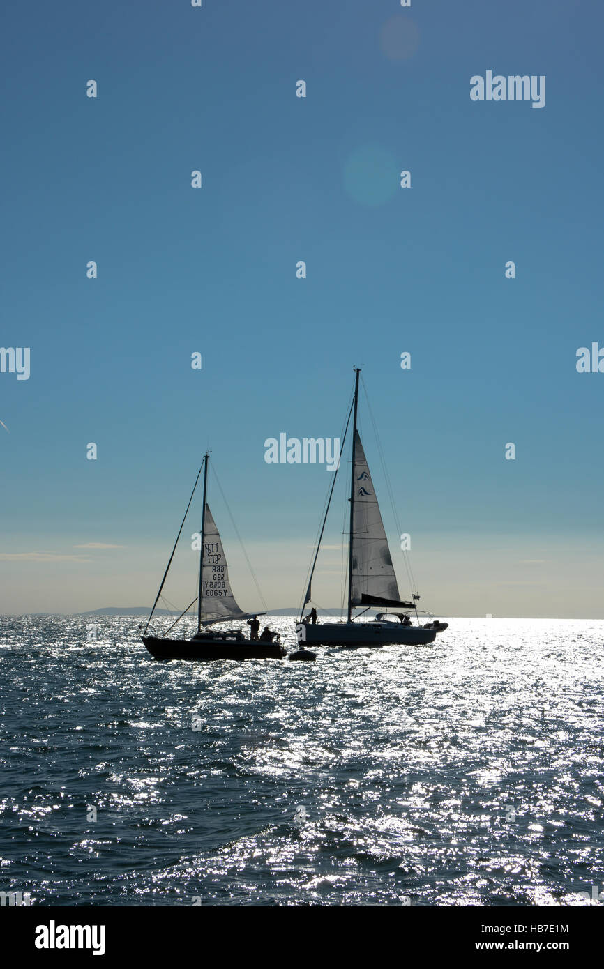 Zwei Yachten in Tenby Bucht vor Anker vorbereiten Segeln auf einem blauen wolkenlosen Himmel und die Sonne auf dem Meer spiegeln. Stockfoto