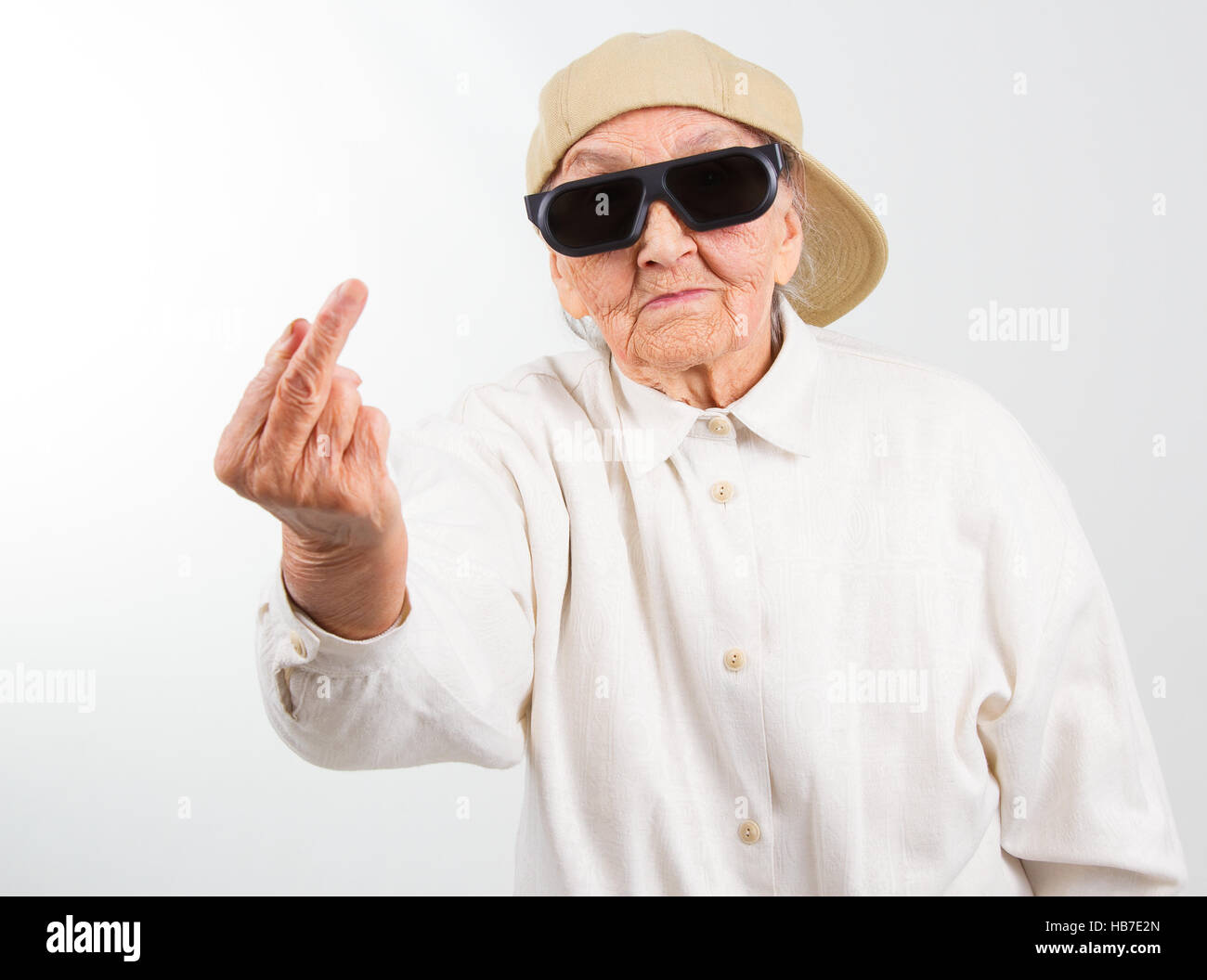 Lustige Oma Studioportrait tragen Brillen und Baseball-Cap, den f-Finger zeigt, isoliert auf weiss Stockfoto
