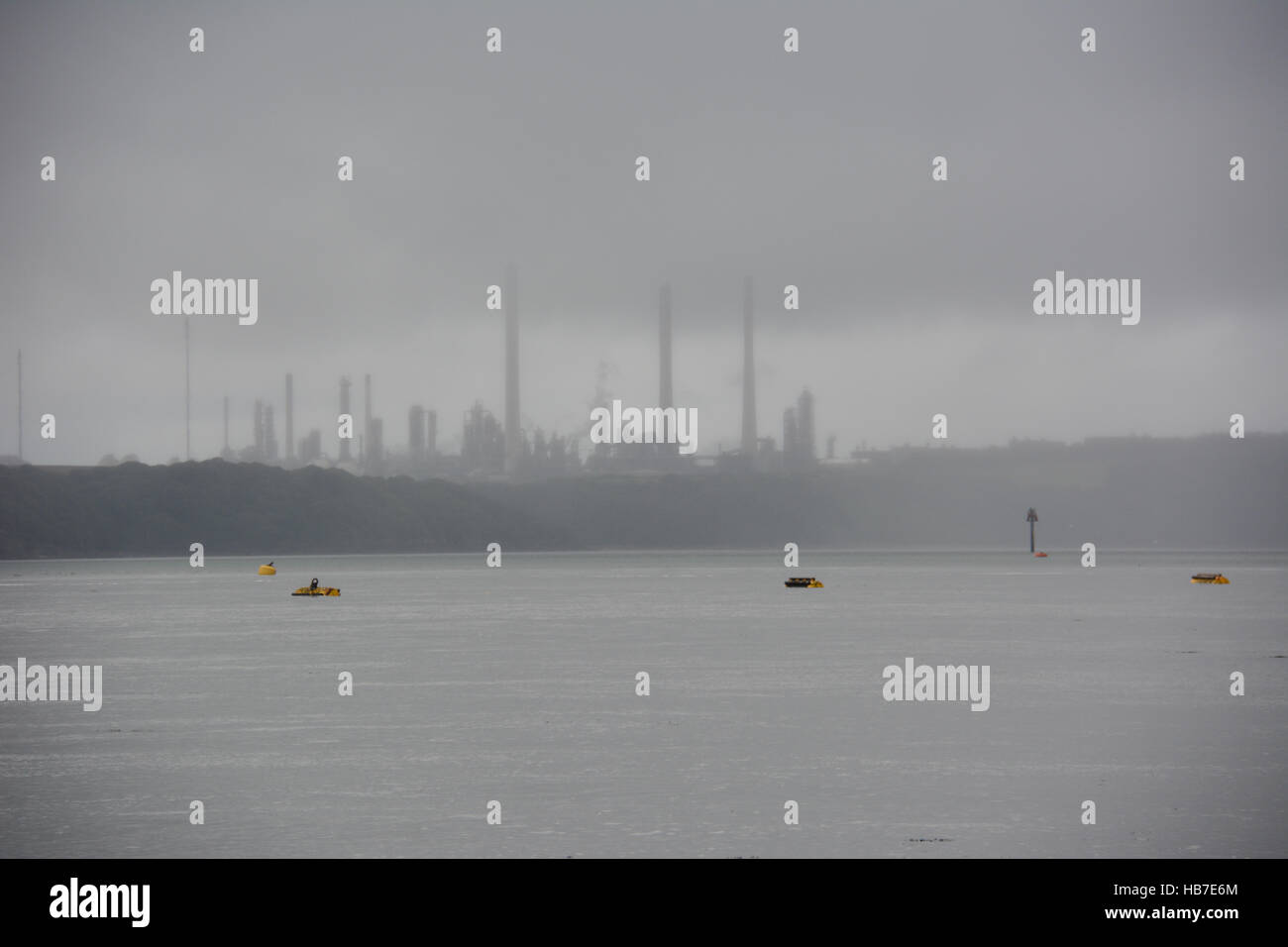 Bojen und Navigation Mark stehend aus einem grauen Meer mit Pembroke Raffinerie fast Silhouette im grauen Nebel Stockfoto