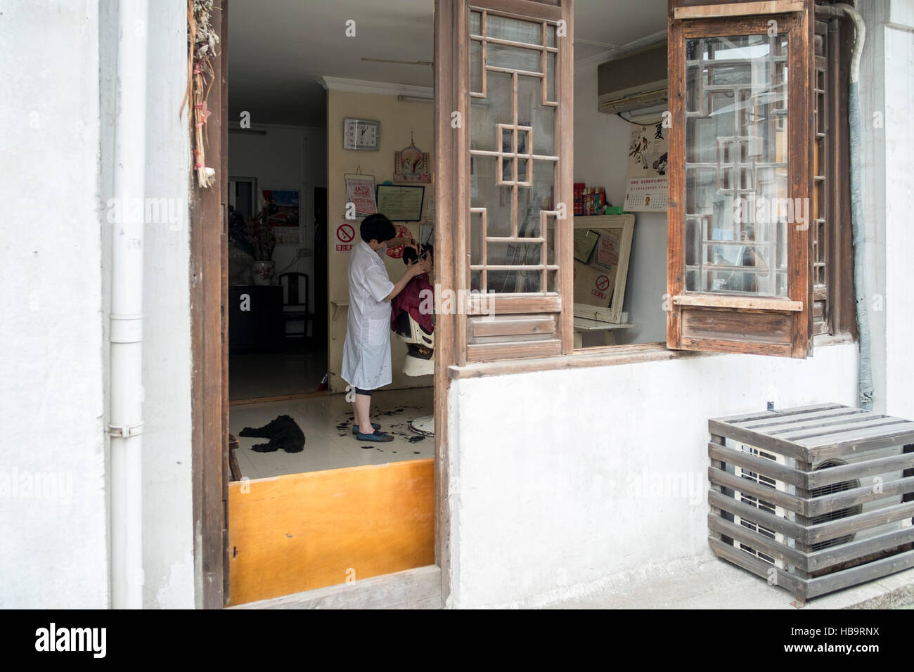 Chinesischen Friseur bei der Arbeit mit einem Klienten an seinem kleinen Friseurladen, Nanxun, Zhejiang, china Stockfoto