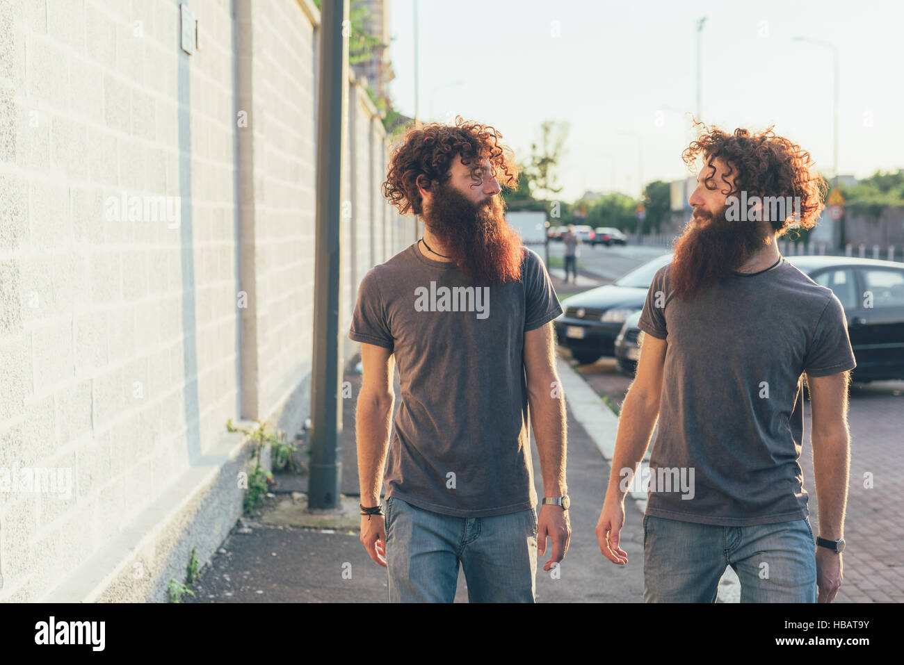 Identische männliche Erwachsene Zwillinge flanieren und im Chat auf Bürgersteig Stockfoto