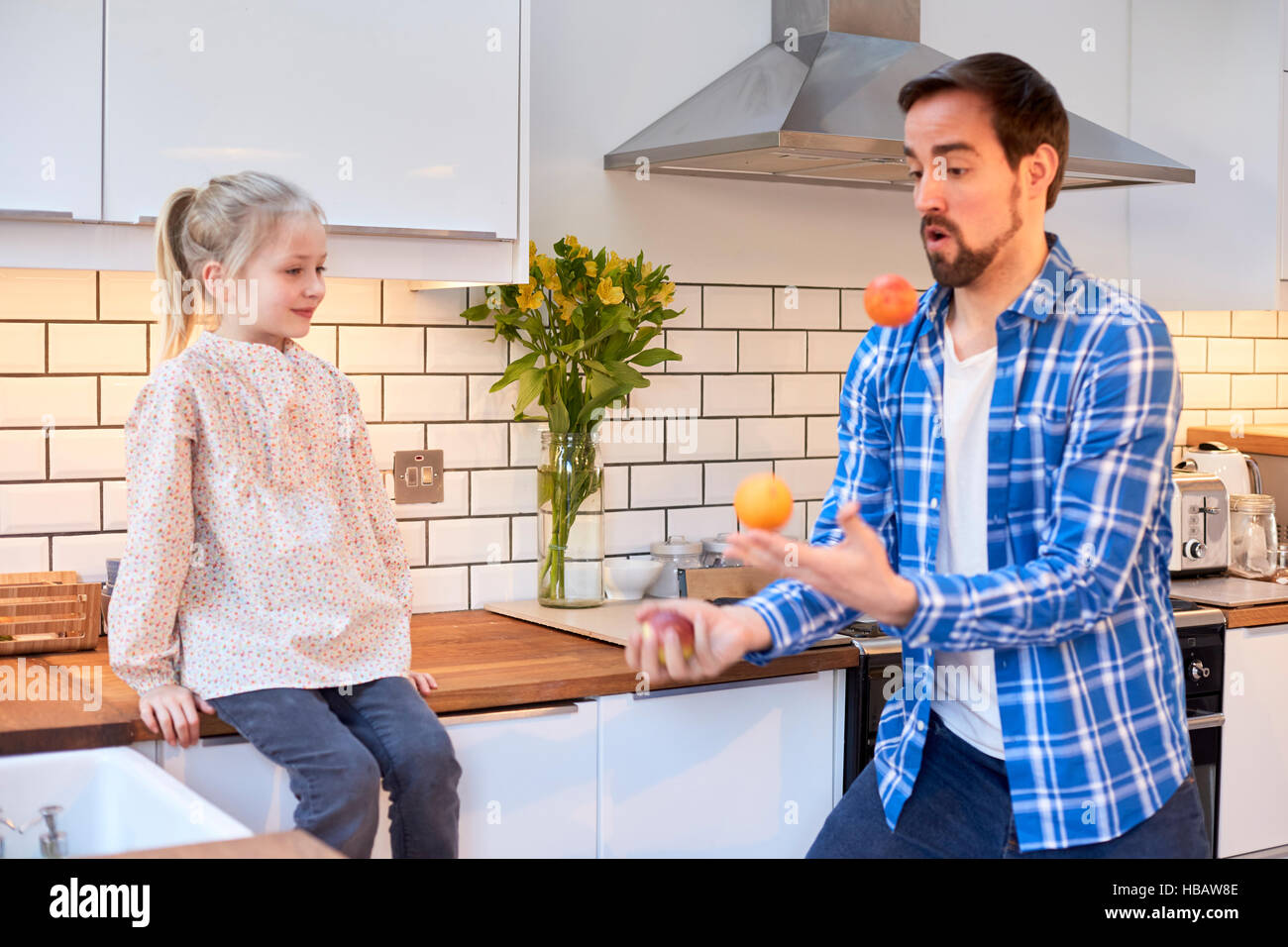 Mitte erwachsenen Mannes jonglieren Obst für Tochter in der Küche Stockfoto