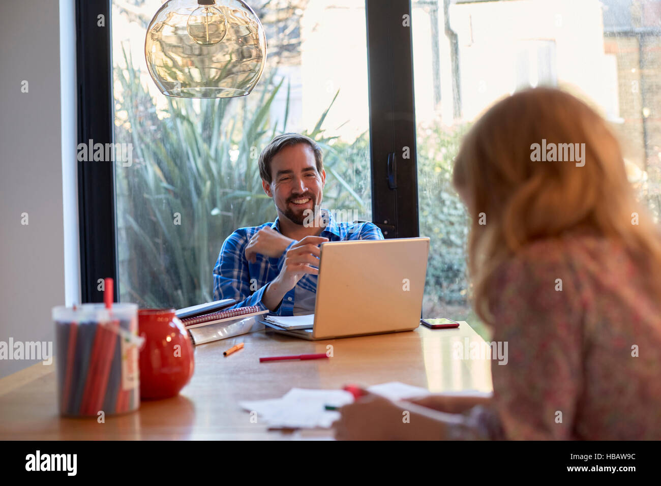 Mitte erwachsener Mann mit Laptop am Esstisch, während Tochter Färbung Stockfoto