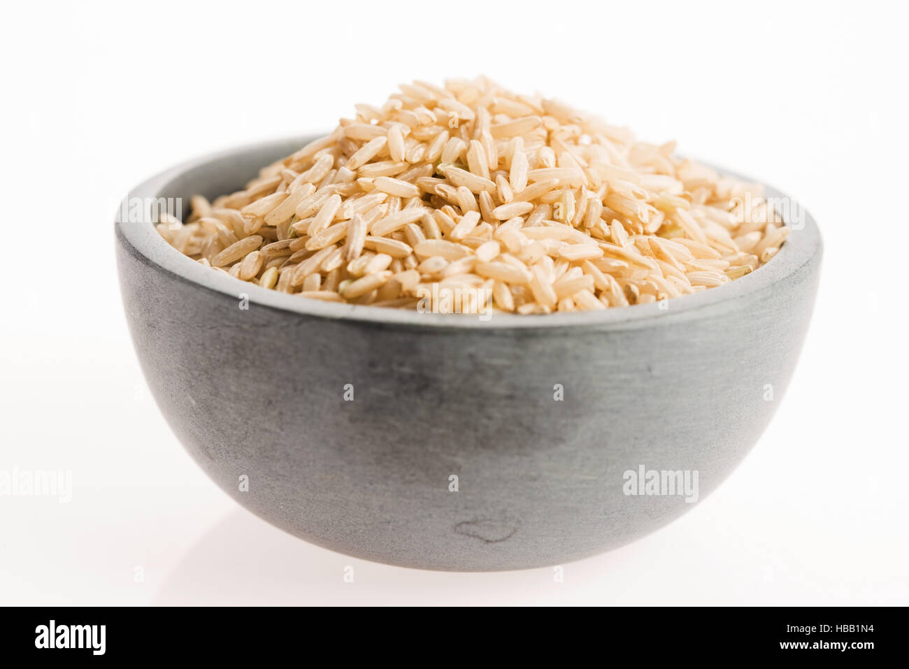 brauner Reis in eine Schüssel geben, die isoliert auf weißem Hintergrund Stockfoto