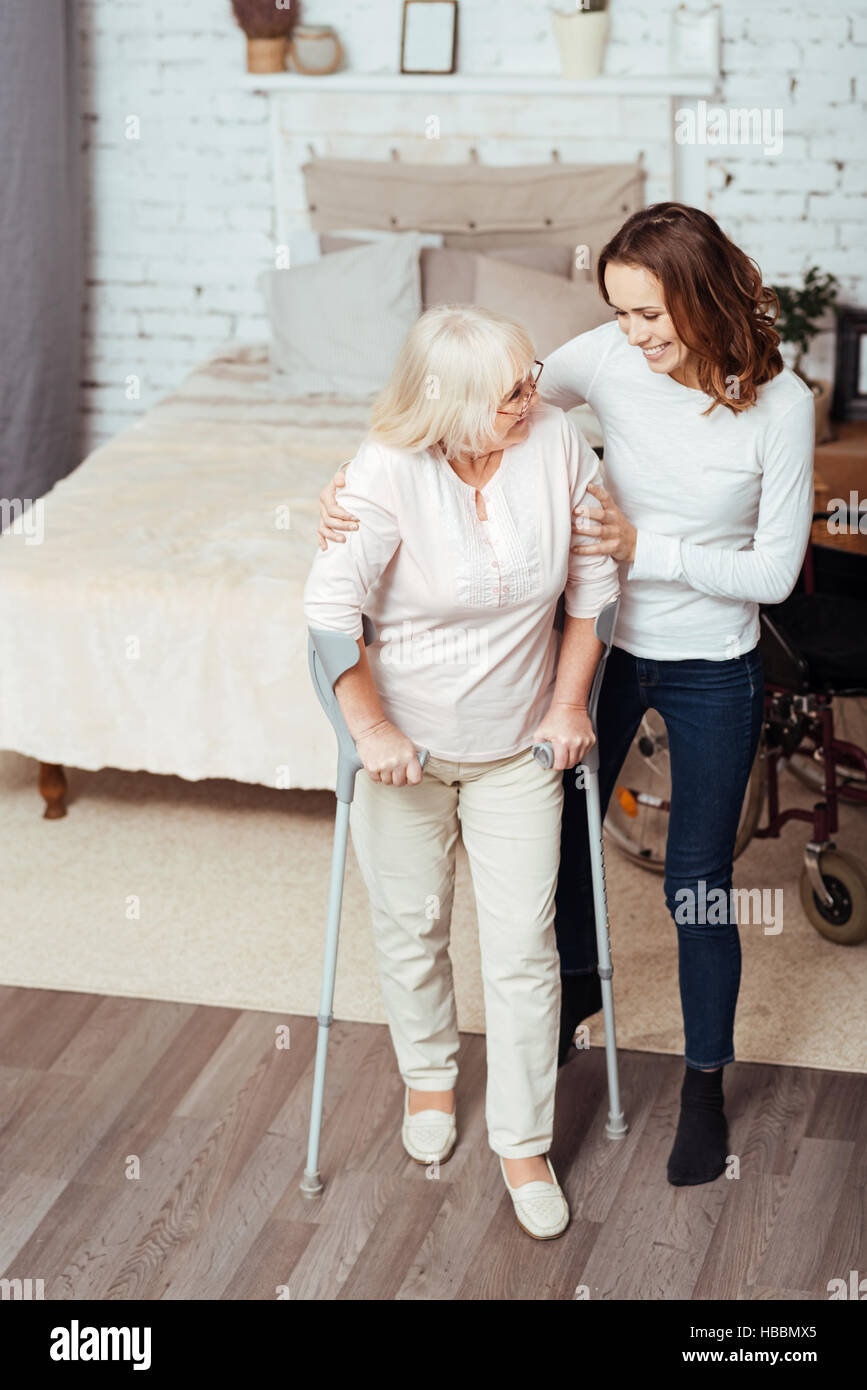 Positiven liebende Frau helfen deaktiviert Oma mit Krücken gehen Stockfoto