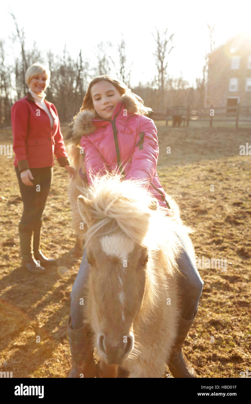 Junges Mädchen reiten Pony, Mutter von hinten beobachten Stockfoto