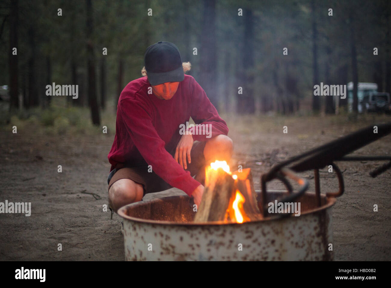 Junger Mann kauert am Lager Feuer im Wald in der Dämmerung, Mammoth Lakes, Kalifornien, USA Stockfoto