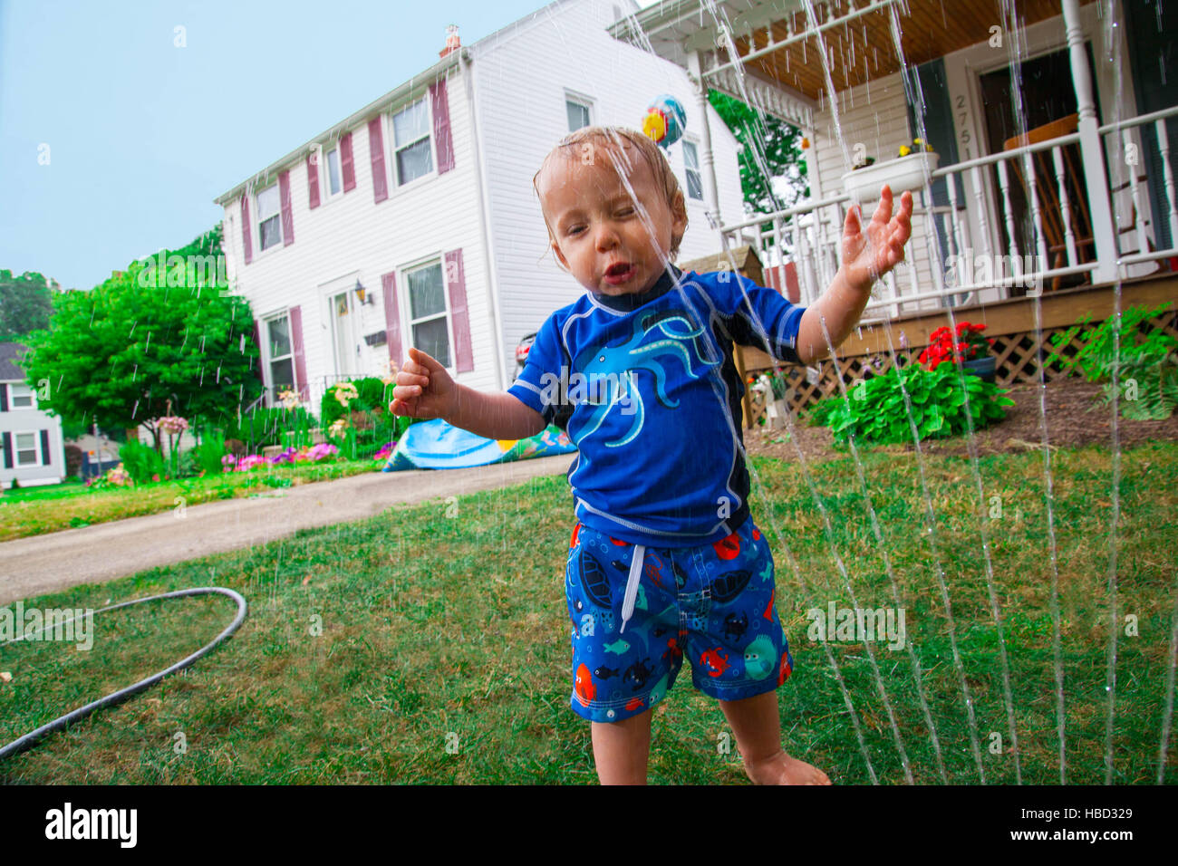 Kaukasische Baby Junge spielt mit einem Wasser-Sprenger in seinem vorderen Rasen im Sommer Stockfoto