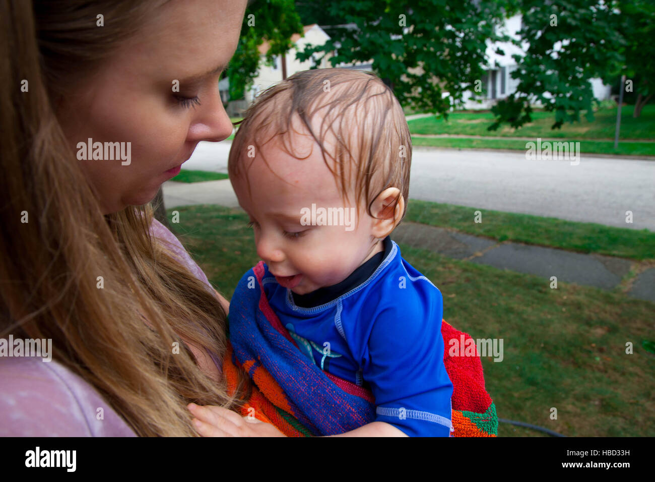 Kaukasischen jungen durch seine Mutter nach dem Spiel mit einem Wasser-Sprenger in seinem vorderen Rasen im Sommer statt Stockfoto